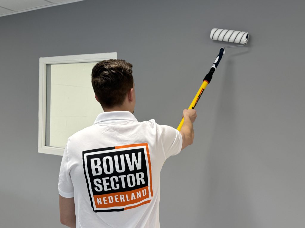 Schilder met het Bouwsector-logo op zijn rug zet de verf strak langs een wit kozijn
