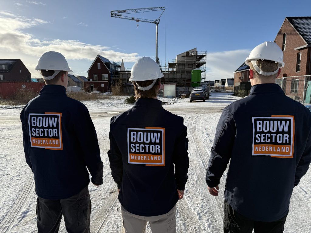Drie vakmensen van Bouwsector Nederland in werkjas kijken op een winterdag naar een straat met nieuwe huizen
